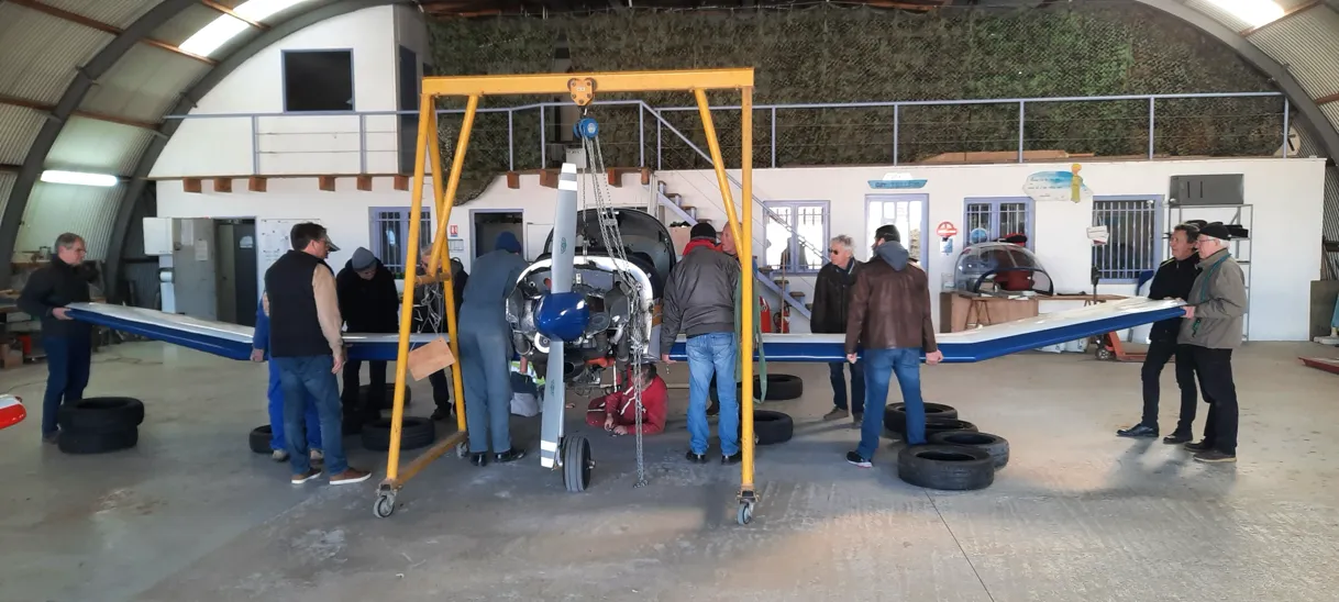 Des bénévoles de l’aéroclub réunis autour d’un avion en maintenance dans le hangar